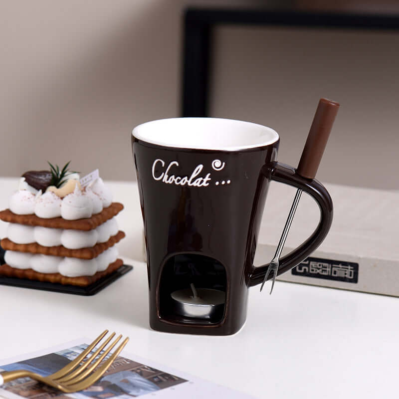 Chocolate fondue mug set with fork, dessert, and tea light on kitchen table