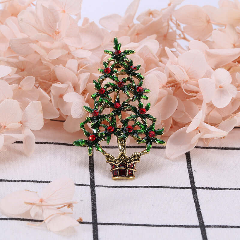 Decorative Christmas tree brooch with green leaves and red accents, floral background
