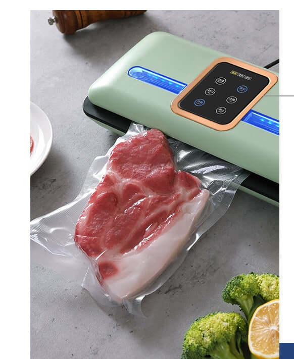 Vacuum sealer machine sealing raw meat in plastic bag on kitchen counter with broccoli and lemon
