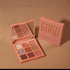 Peach-toned eyeshadow palette with mirror, featuring shimmer and matte shades, on brown background