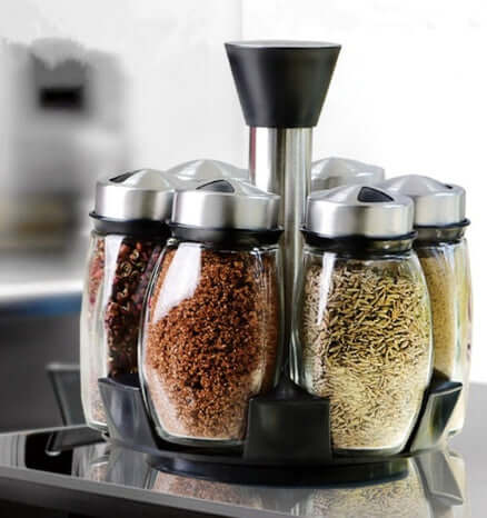 Rotating spice rack organizer with glass jars and stainless steel lids on kitchen counter