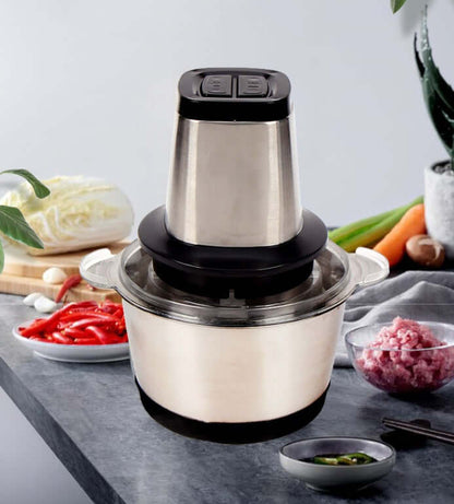 Stainless steel electric food chopper on kitchen counter with vegetables and meat