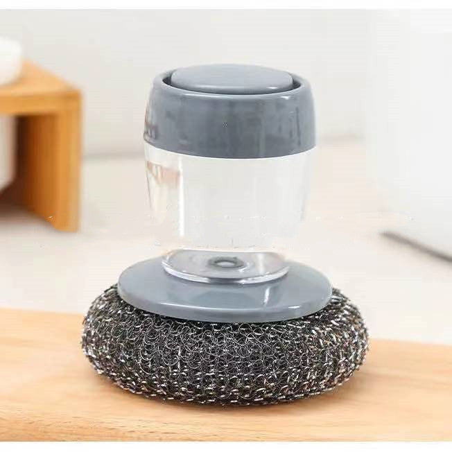 Kitchen soap dispensing scrubber with metal scouring pad on wooden surface