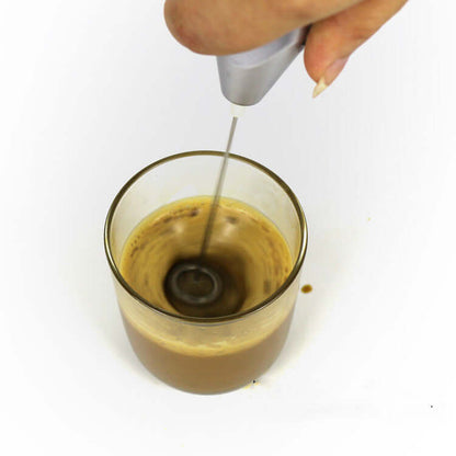 Handheld milk frother mixing coffee in glass cup on white background