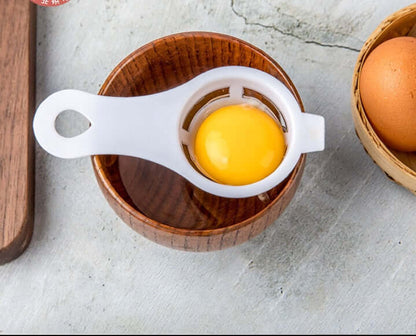 Egg separator kitchen tool with egg yolk over wooden bowl, egg in basket nearby