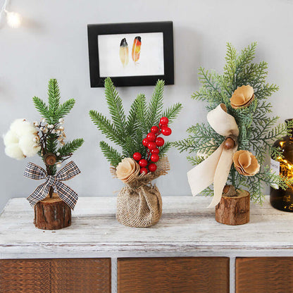 Mini artificial Christmas trees with berries, pine branches, and rustic bows on a white table.