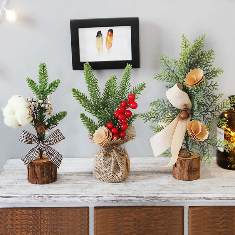 Three small artificial Christmas tree decorations with pine branches and festive accents on a wooden table