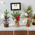 Three small artificial Christmas tree decorations with pine branches and festive accents on a wooden table