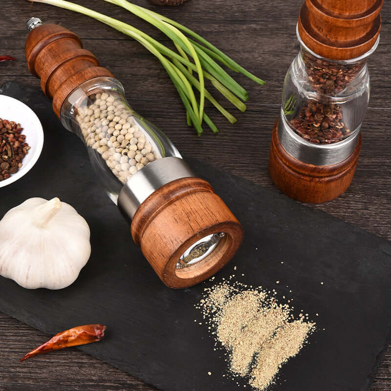 Wooden pepper grinder and spice mill on a slate tray with garlic, chili, and green onions.