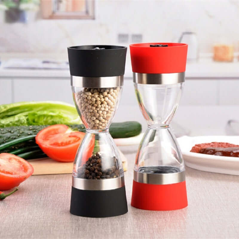 Dual manual spice grinders with black and red bases on kitchen countertop with vegetables