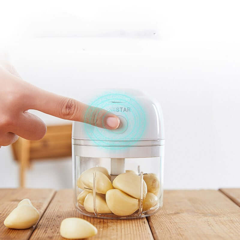 Hand pressing button on electric garlic chopper filled with garlic cloves on kitchen table