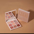 Pink and gold eyeshadow palette with mirror, featuring matte and glitter shades on beige background.