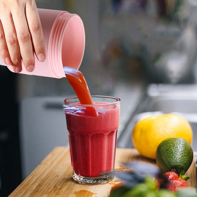 Hand pouring fresh red fruit smoothie into glass on kitchen counter with fruits nearby