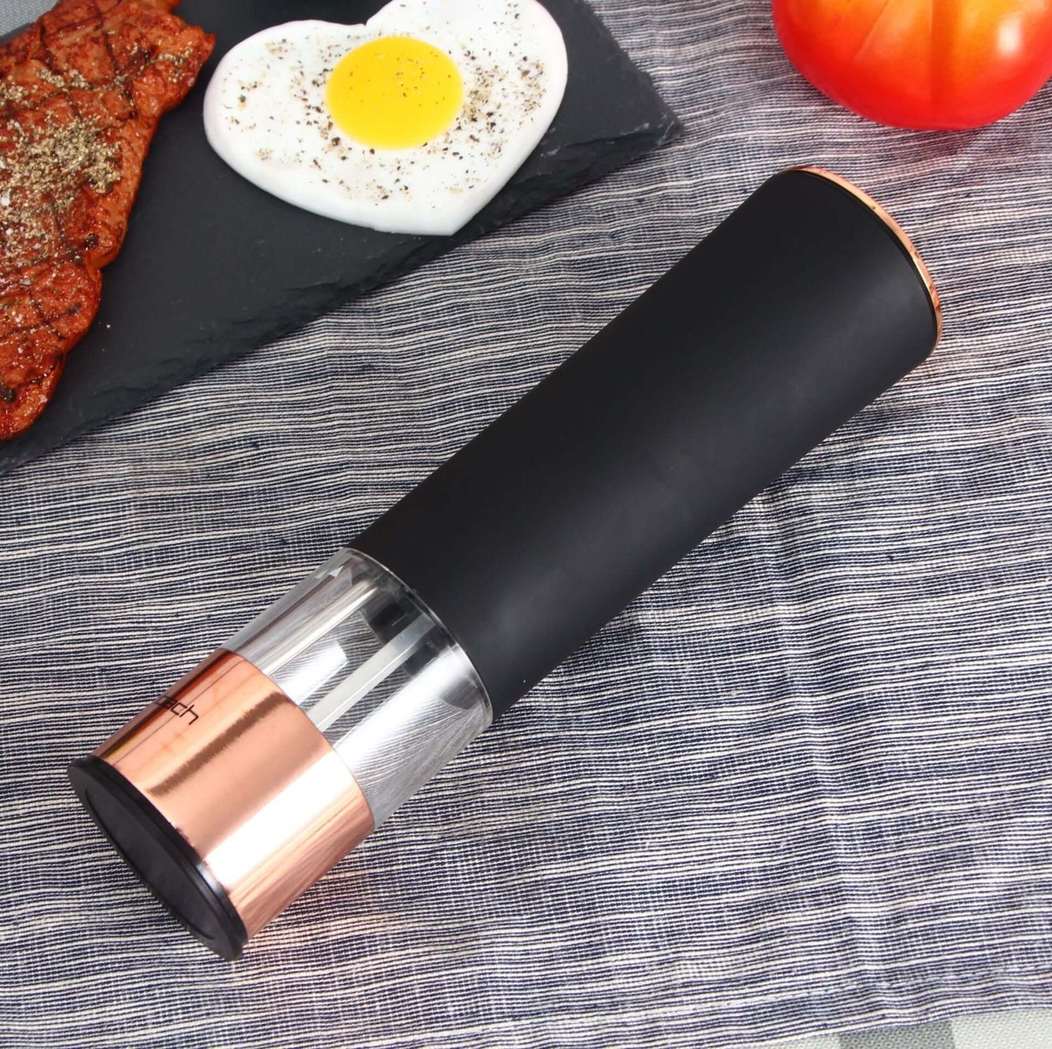 Electric pepper grinder with black and rose gold design on a kitchen table near steak and egg