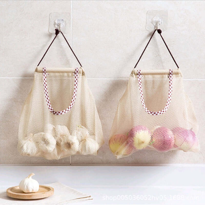Reusable mesh produce bags hanging on wall, storing garlic and apples in a kitchen setting