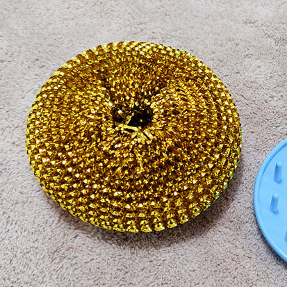 Gold metal kitchen scrubber on a beige surface with blue plastic part nearby