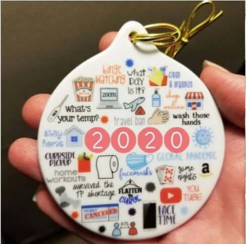 Hand holding a 2020-themed ceramic ornament with pandemic icons and phrases, kitchen accessory