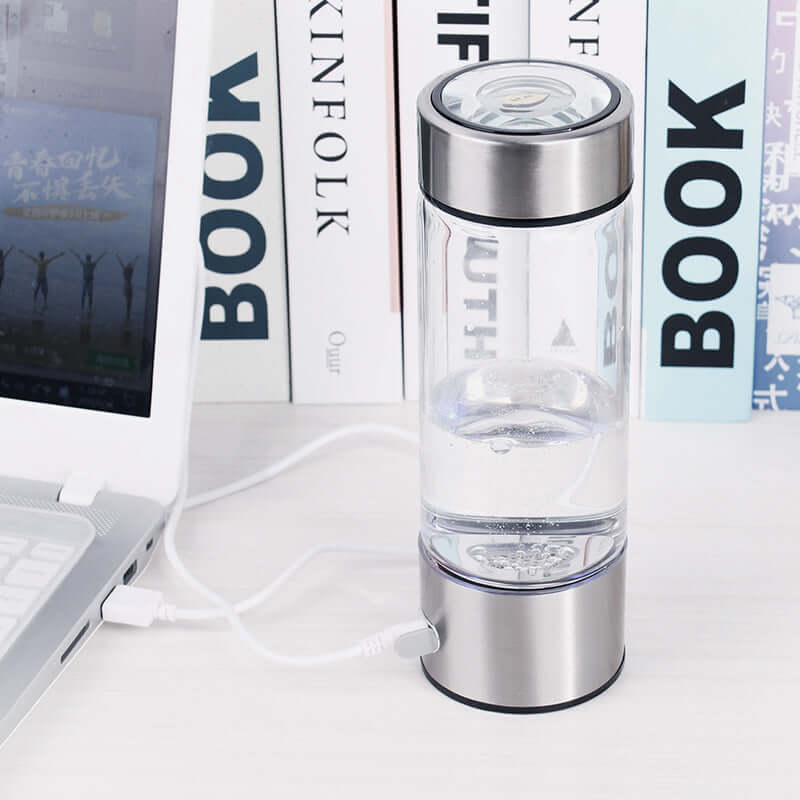 Portable hydrogen water bottle with stainless steel lid, USB charging, on a desk with books.