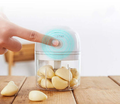 Electric garlic chopper with garlic cloves inside on a wooden kitchen table, hand pressing top button