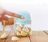 Electric garlic chopper with garlic cloves inside on a wooden kitchen table, hand pressing top button