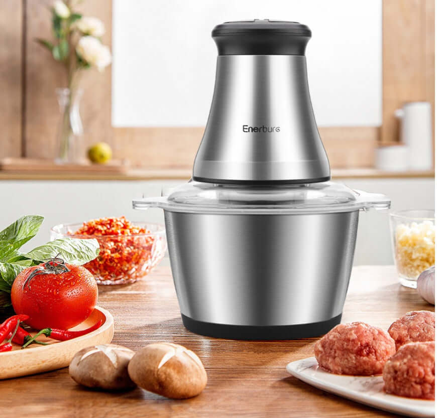 Stainless steel electric food chopper on kitchen counter with fresh vegetables and meatballs