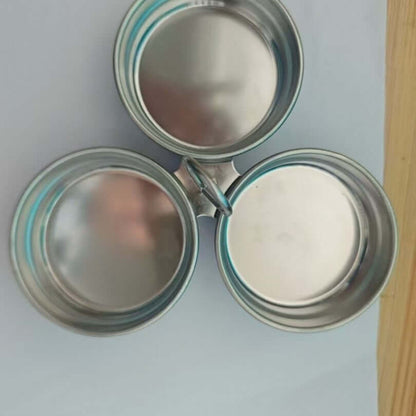Three round stainless steel spice containers with lids joined by a central ring on a table.