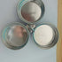 Three round stainless steel spice containers with lids joined by a central ring on a table.