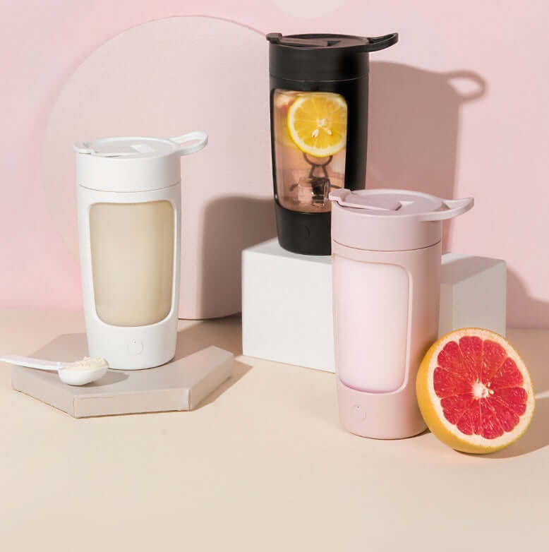 Three portable blender bottles in black, white, and pink, with fruit and protein powder