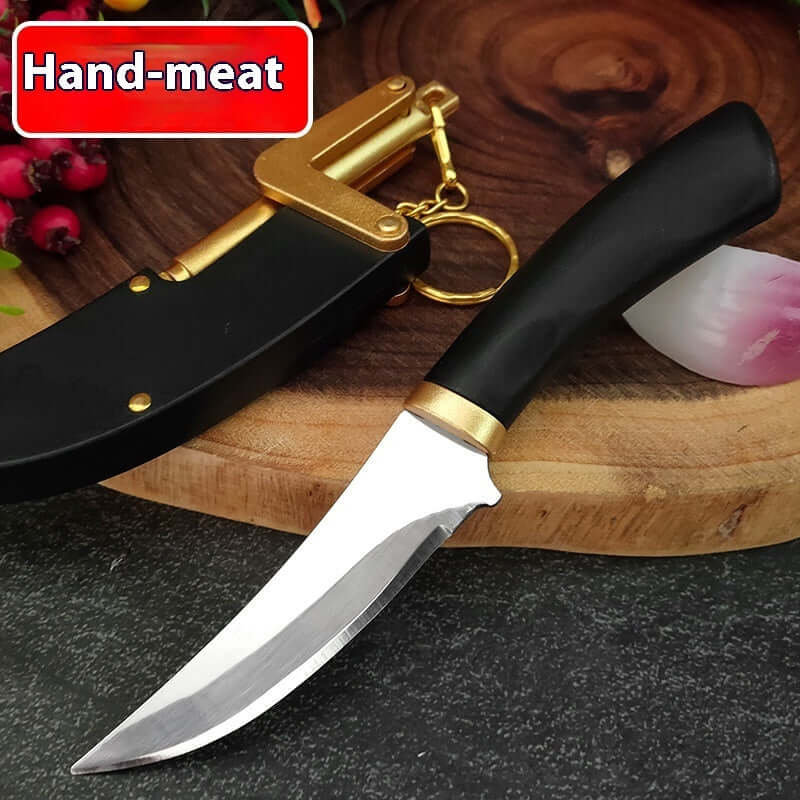 Curved kitchen knife with black handle and gold bolster on wood board, black sheath beside