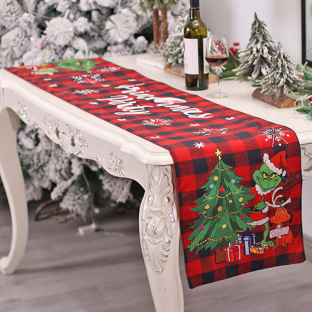 Red plaid Christmas table runner with Grinch and tree design on a white festive table.