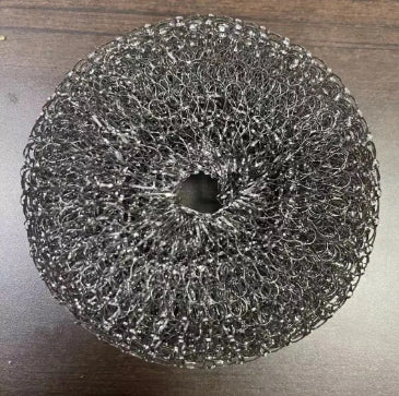 Black metal mesh kitchen scrubber on a dark wooden surface, round cleaning accessory