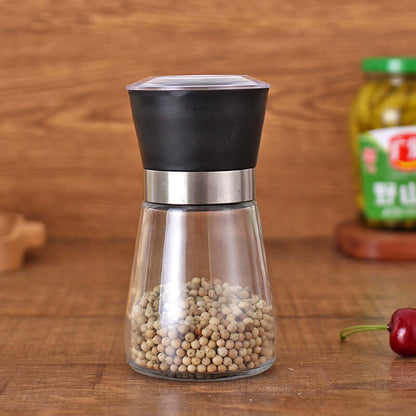 Glass and stainless steel pepper grinder filled with whole peppercorns on a kitchen counter