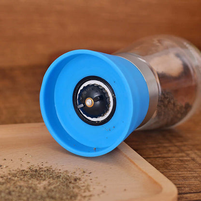 Manual pepper grinder with blue lid, stainless steel base, and ground pepper on a wooden board
