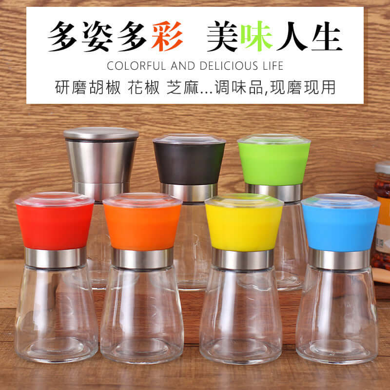 Set of six colorful glass spice grinders with stainless steel tops on a wooden kitchen counter