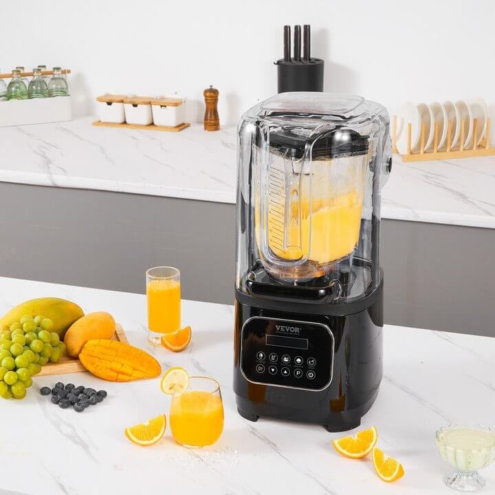 Countertop blender making orange juice surrounded by fresh fruit and glasses in modern kitchen