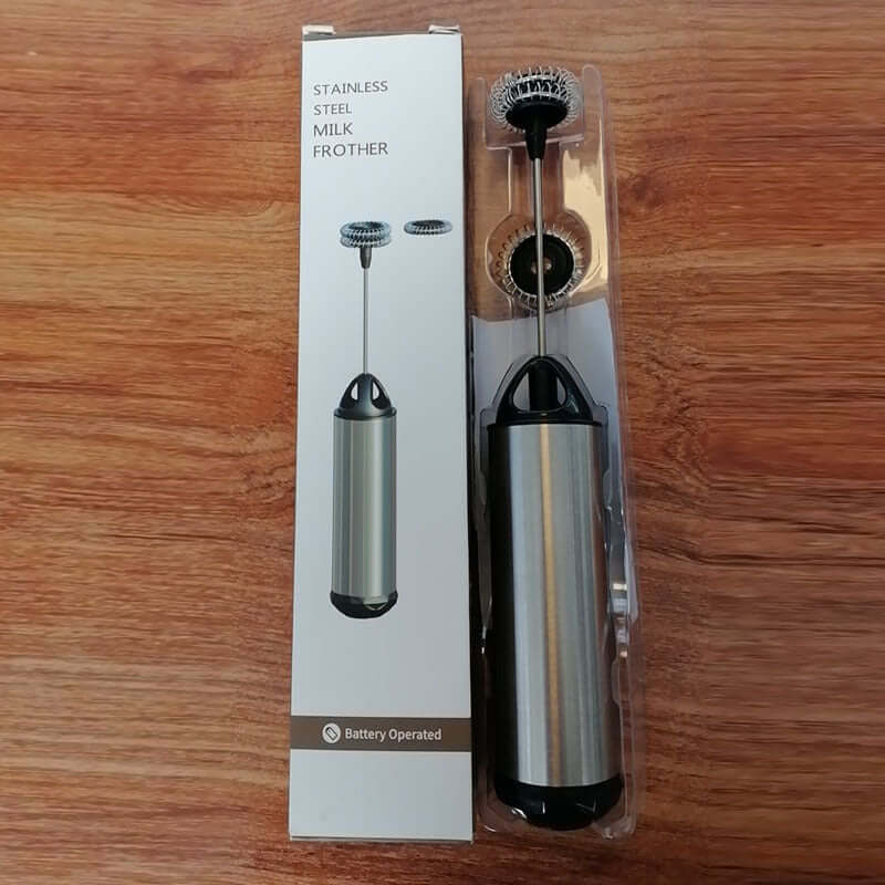 Stainless steel battery-operated milk frother with packaging on wooden surface