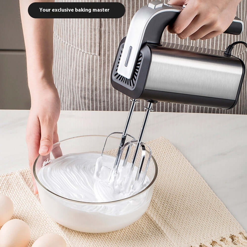 Electric hand mixer beating egg whites in glass bowl on kitchen counter