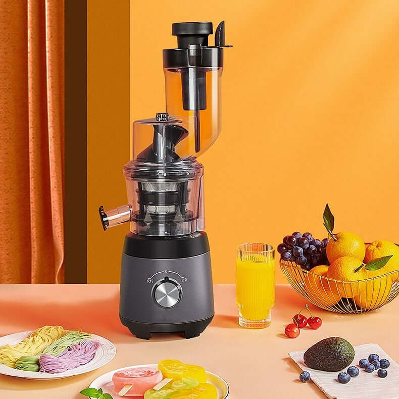 Black juicer machine on kitchen counter with glass of juice, fruits, and colorful noodles.