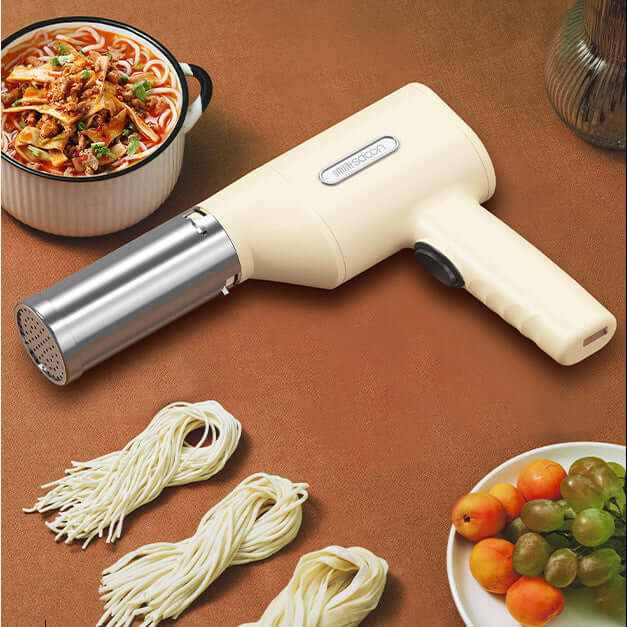 Electric pasta maker with dough noodles, fresh fruit, and bowl of noodle soup on a kitchen table