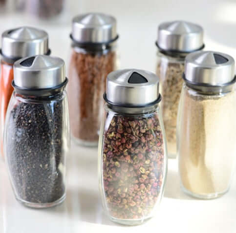 Set of six glass spice jars with metal lids filled with assorted spices on a kitchen counter
