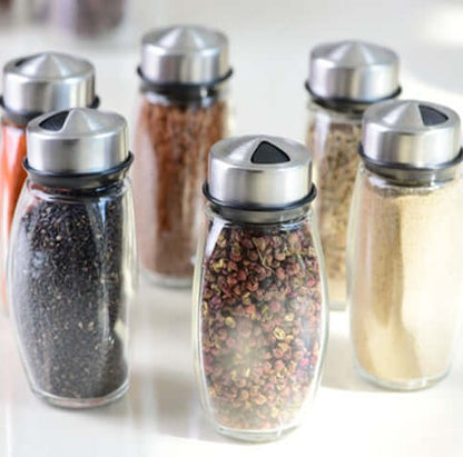 Set of six glass spice jars with metal lids filled with assorted spices on a kitchen counter