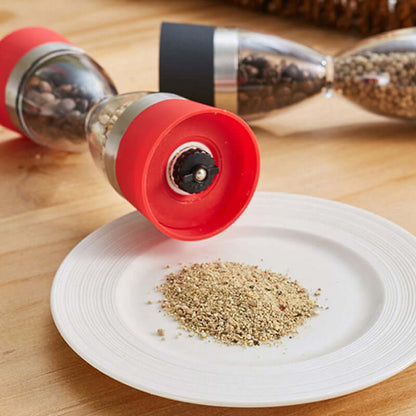 Dual manual spice grinder with red and black ends, grinding pepper onto a white plate