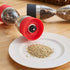 Dual manual spice grinder with red and black ends, grinding pepper onto a white plate