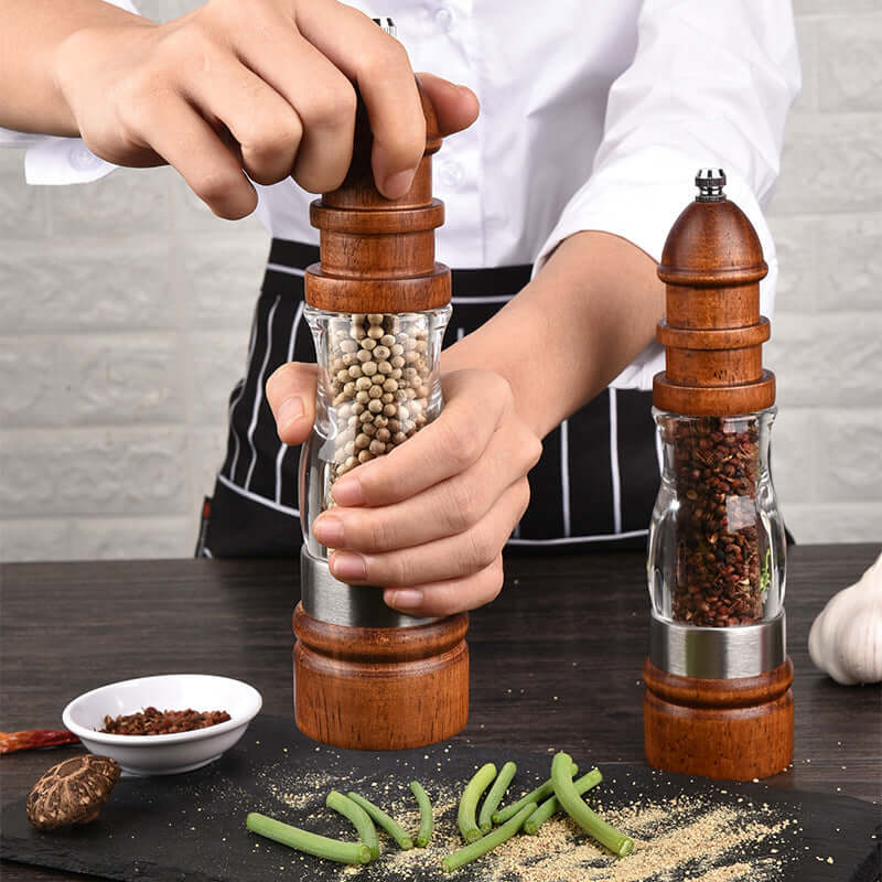 Hand using wooden pepper grinder in kitchen with spices and vegetables on table
