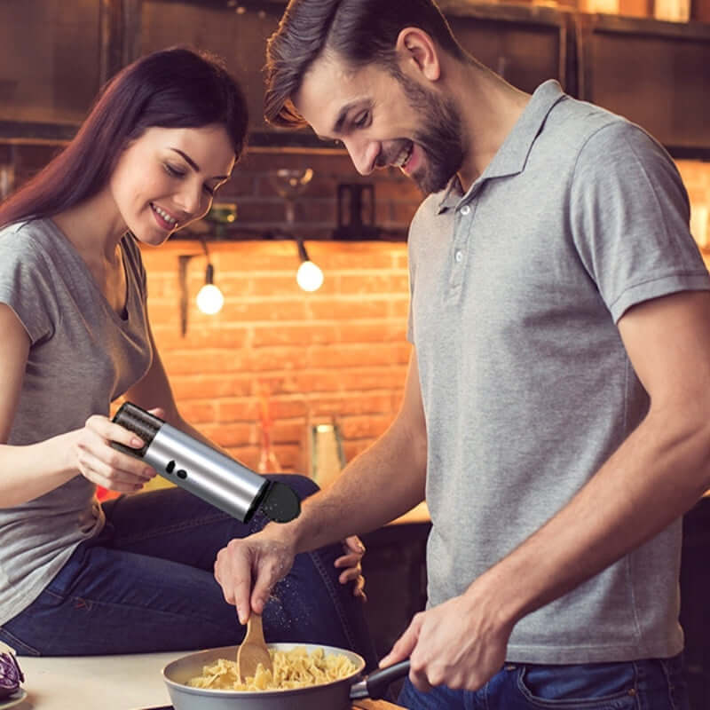 Couple using stainless steel kitchen gadget to season food while cooking pasta