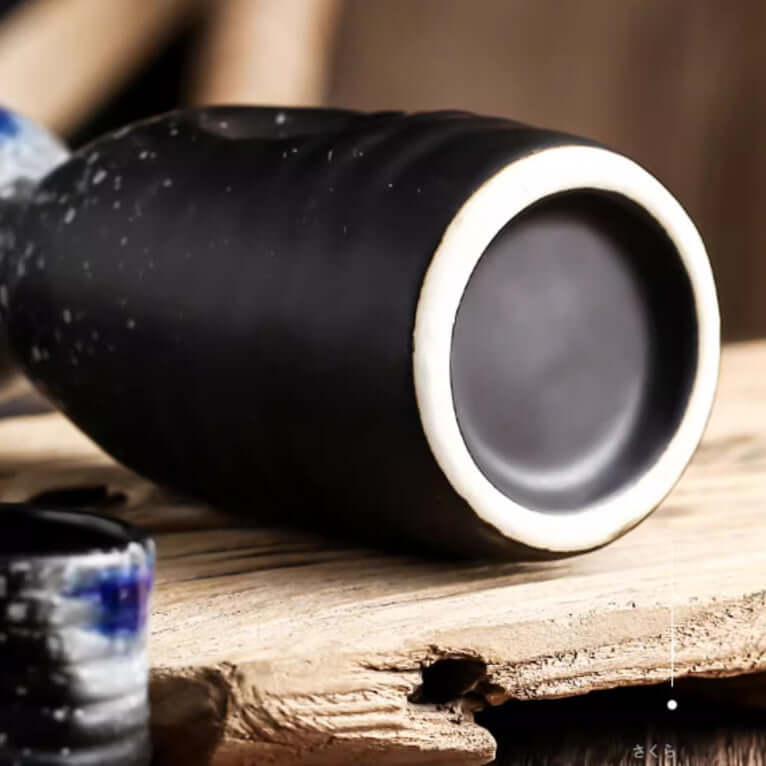 Matte black ceramic cup with white rim on rustic wooden surface, minimalist kitchen accessory