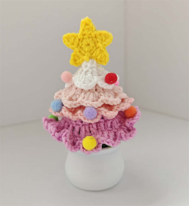 Colorful crochet Christmas tree with a yellow star topper and pom pom ornaments in a white pot
