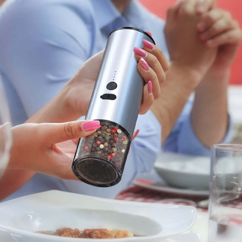 Hand holding electric pepper grinder over plate, modern kitchen accessory on dining table