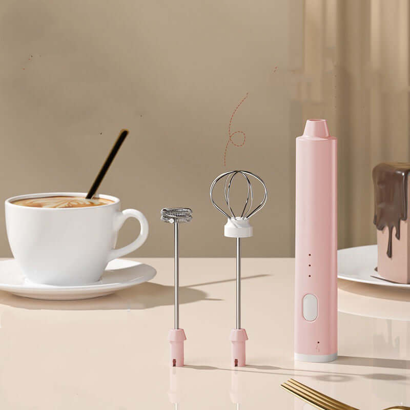 Pink handheld milk frother with two whisk attachments on kitchen counter, coffee in background