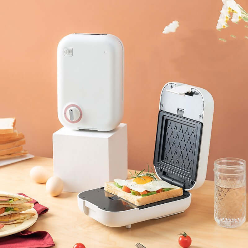 Compact sandwich maker with toasted bread, fried egg, and vegetables on kitchen table